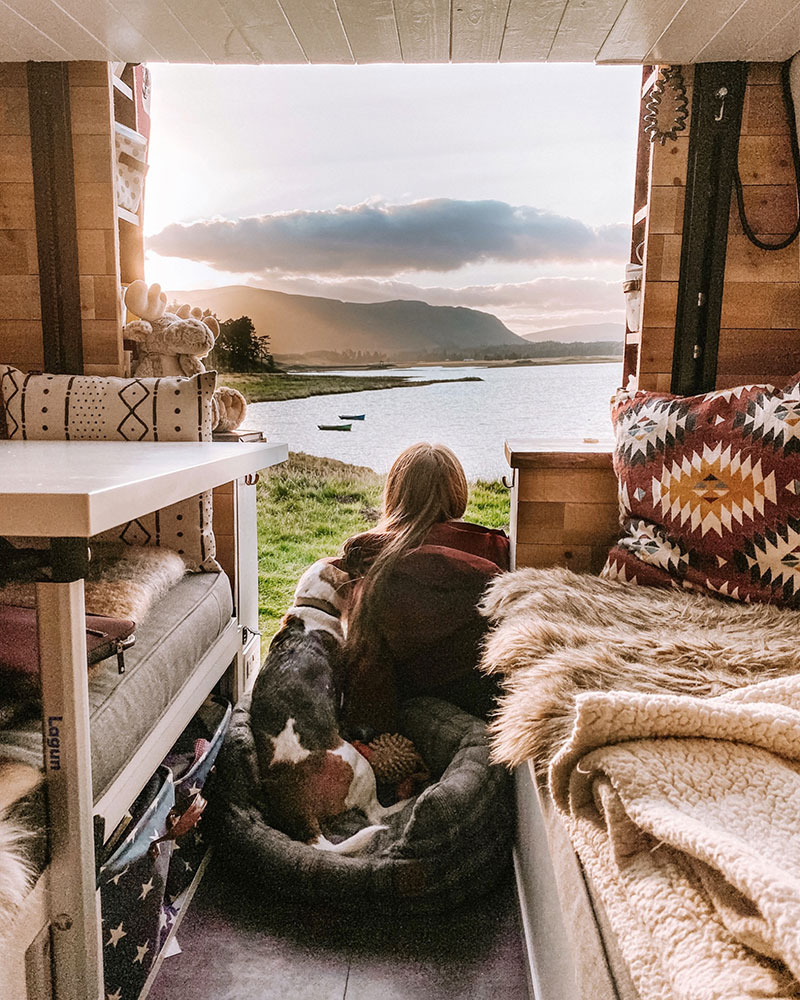 Woman sitting with beagle in campervan watching the sun set over a Scottish loch