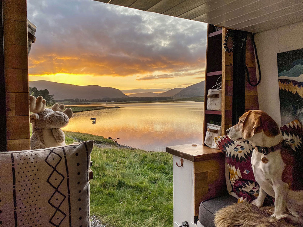 View out of the back of our campervan showing sunset over a loch whilst wild camping in the Scottish Highlands